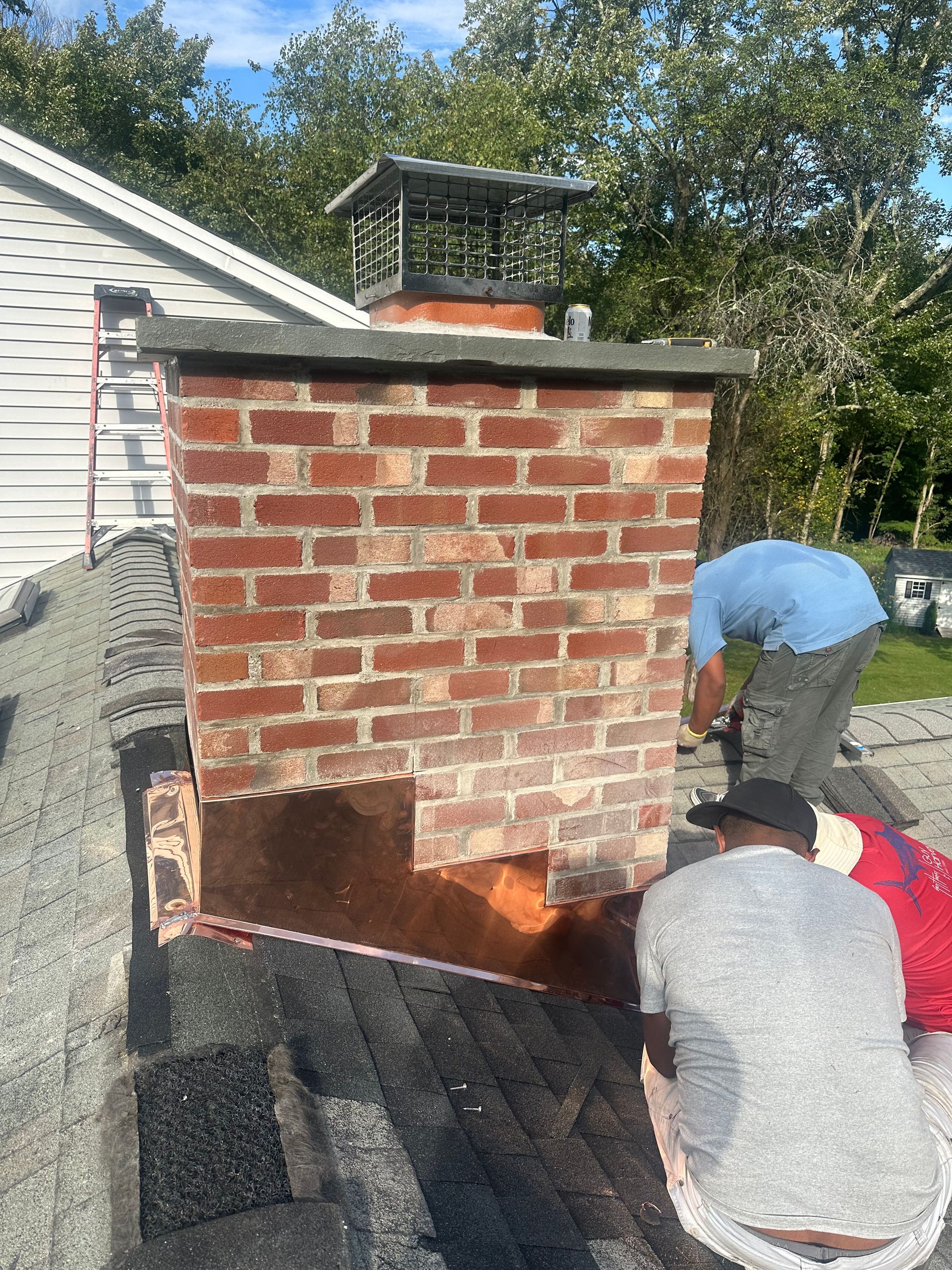 Two people on a roof repairing a section of a brick chimney where the masonry has been removed.