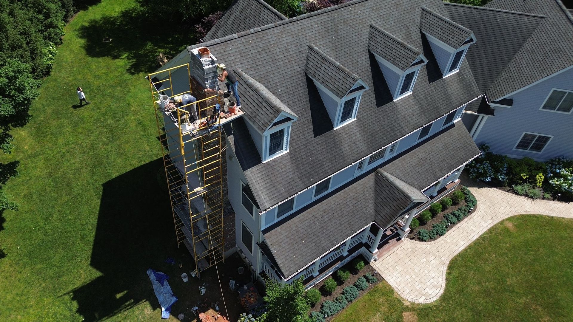 An aerial view of a house with scaffolding set up around a chimney on the side of the roof for construction work.