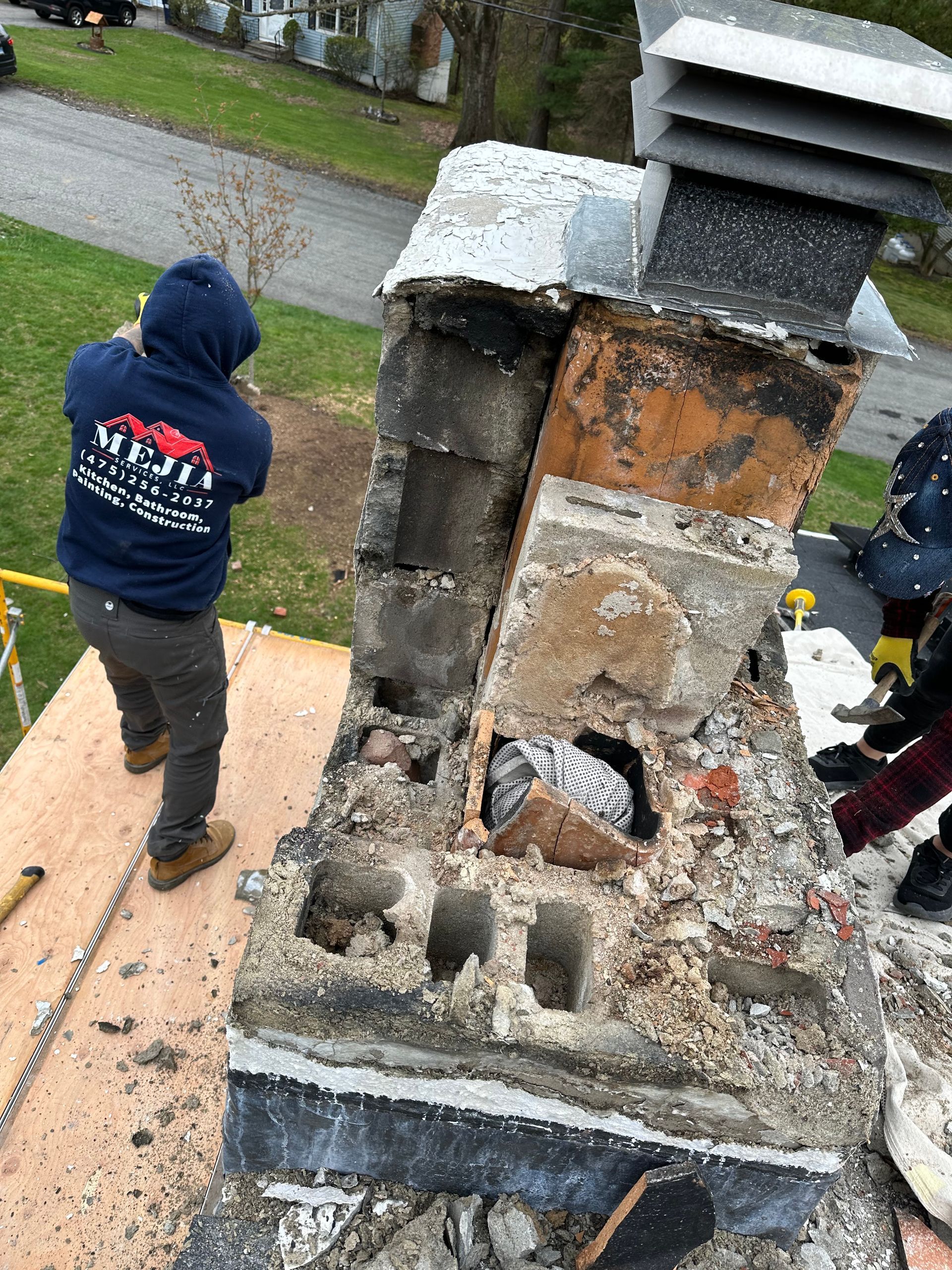 Workers in workwear dismantle a stone chimney stack on a residential roof.