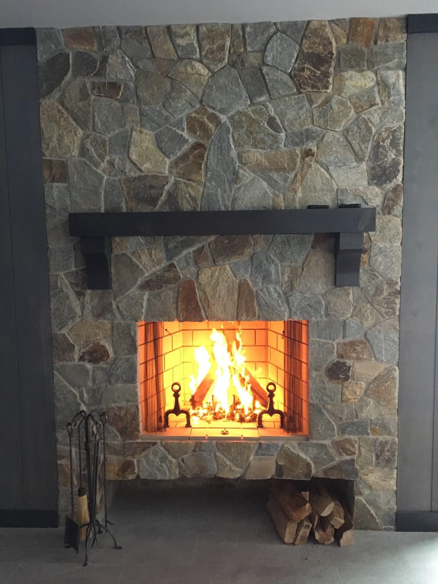 A stone fireplace features a burning fire, a dark wooden mantel, and a built-in log storage cubby at the bottom.