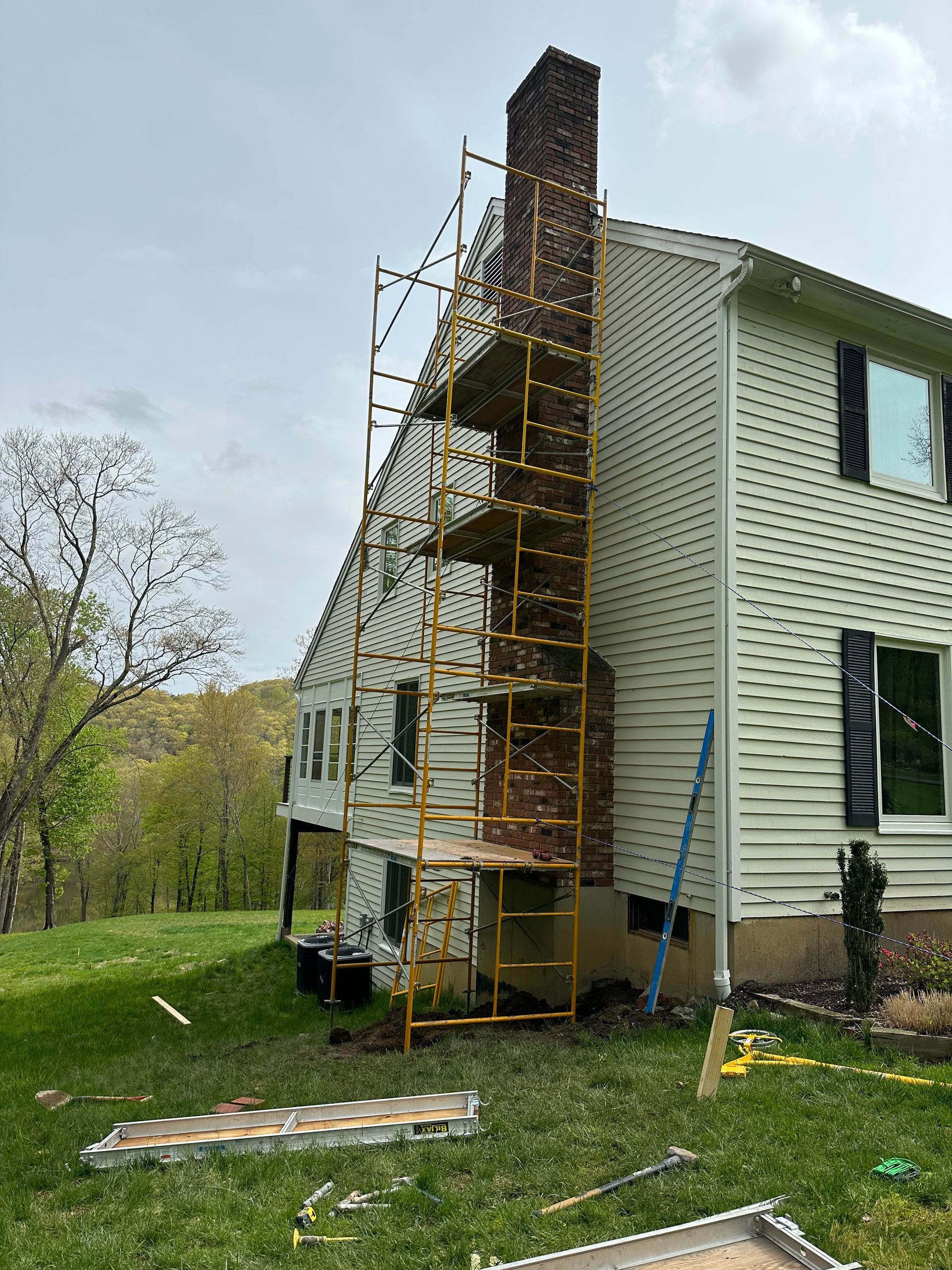 Yellow scaffolding erected along the side of a house to access a tall brick chimney.