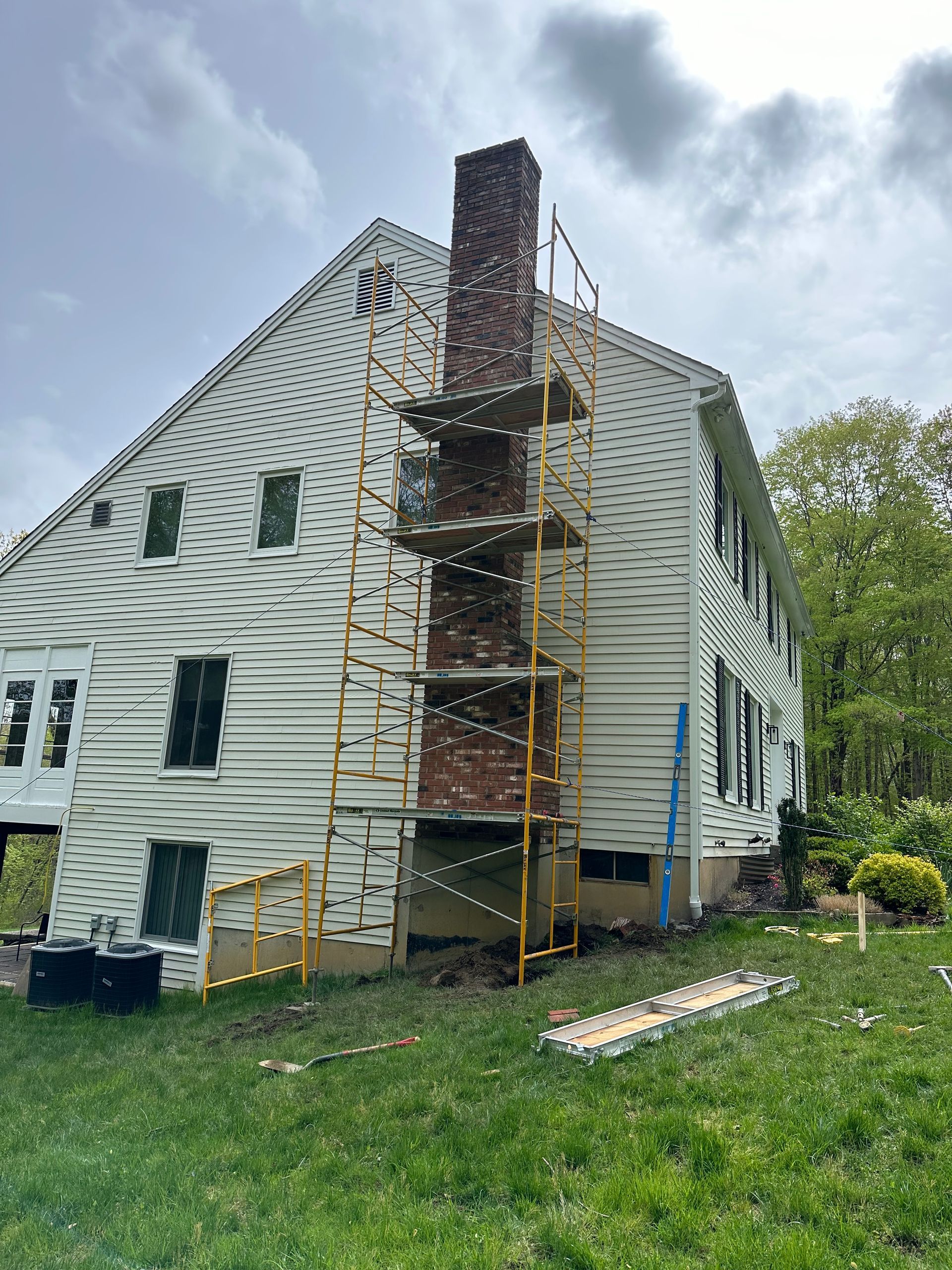 A multi-story house with white siding and a brick chimney under repair, featuring yellow scaffolding against the wall.