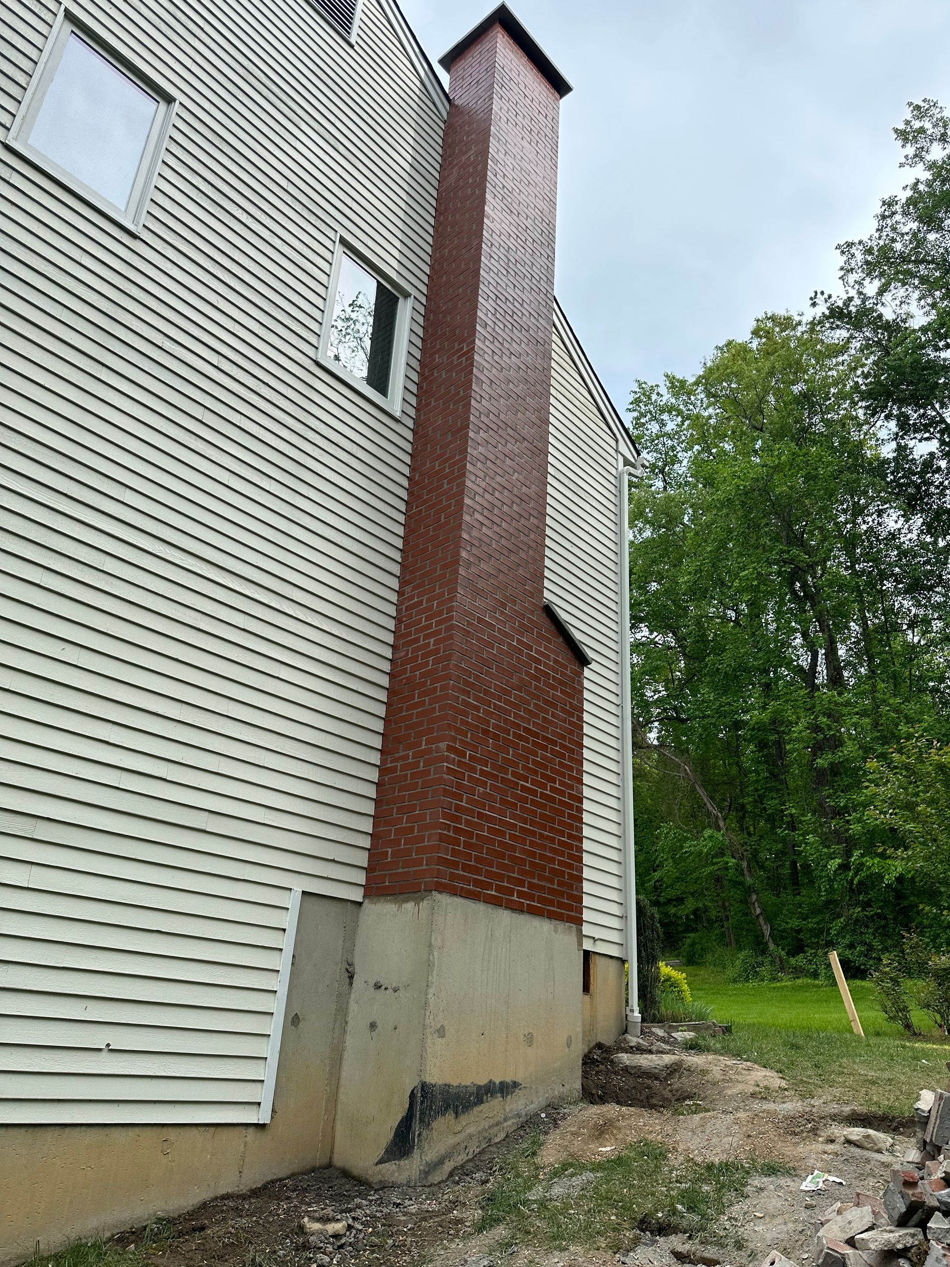Side view of a house with cream-colored siding and a brick chimney exterior against a backdrop of trees.