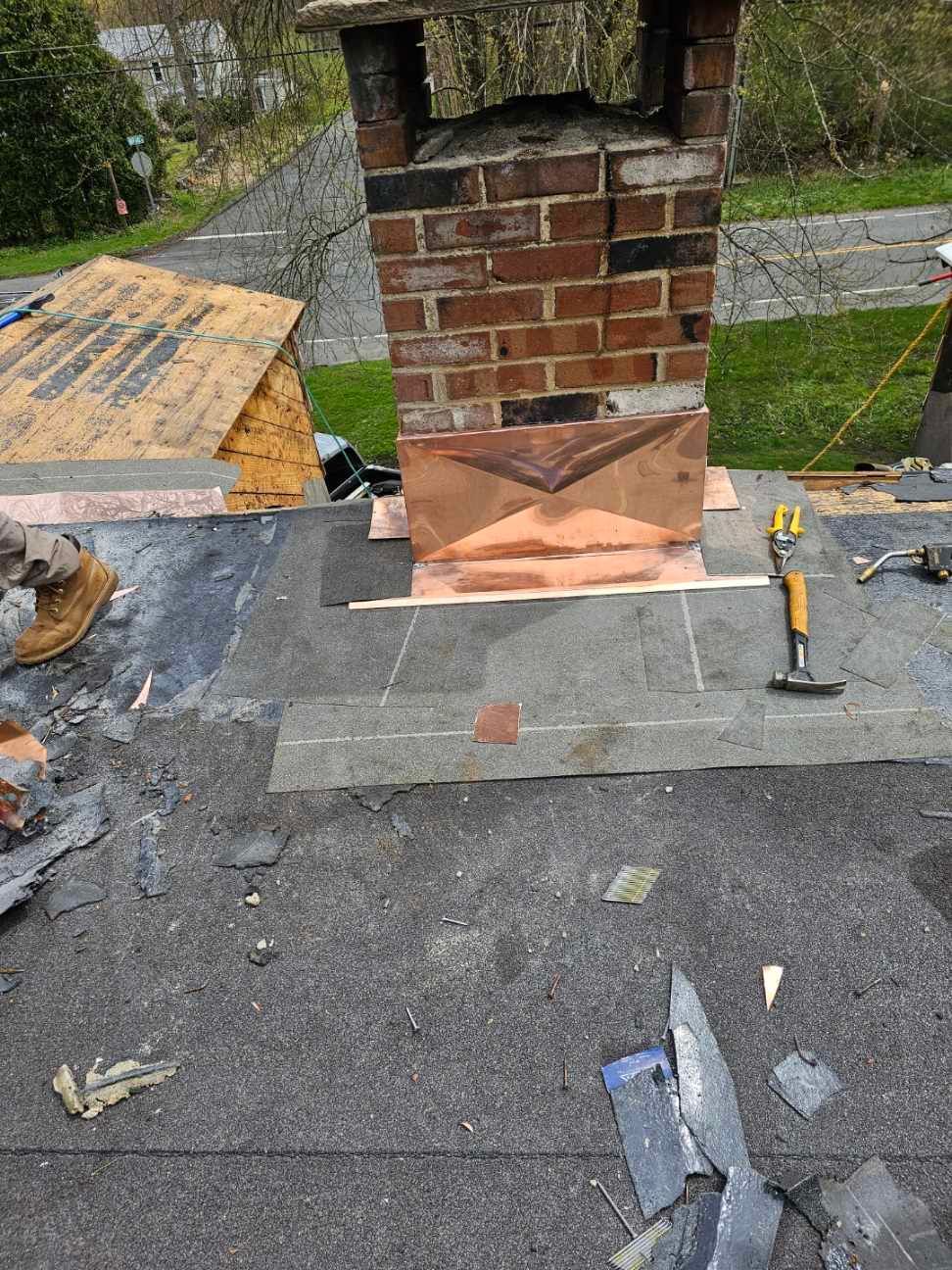 Copper flashing installed around the base of a brick chimney on a partially re-roofed house.