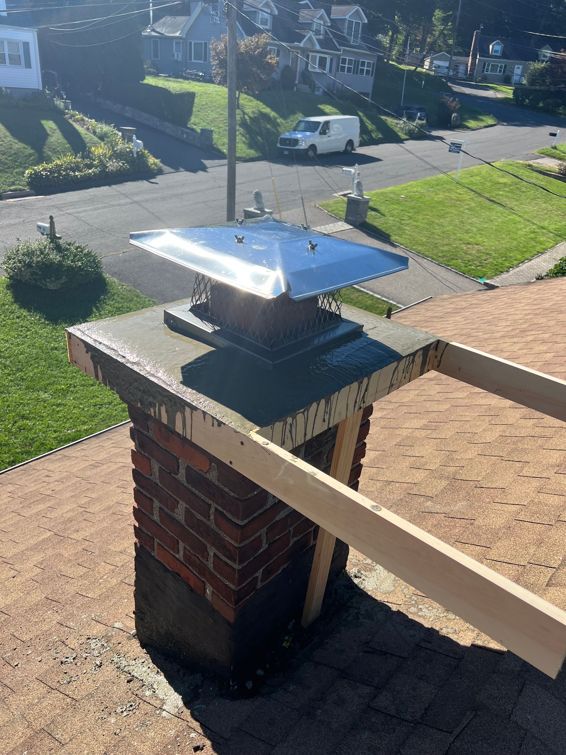 A brick chimney topped with a new concrete crown and a metal flue cap, with wooden forms still attached to the sides.