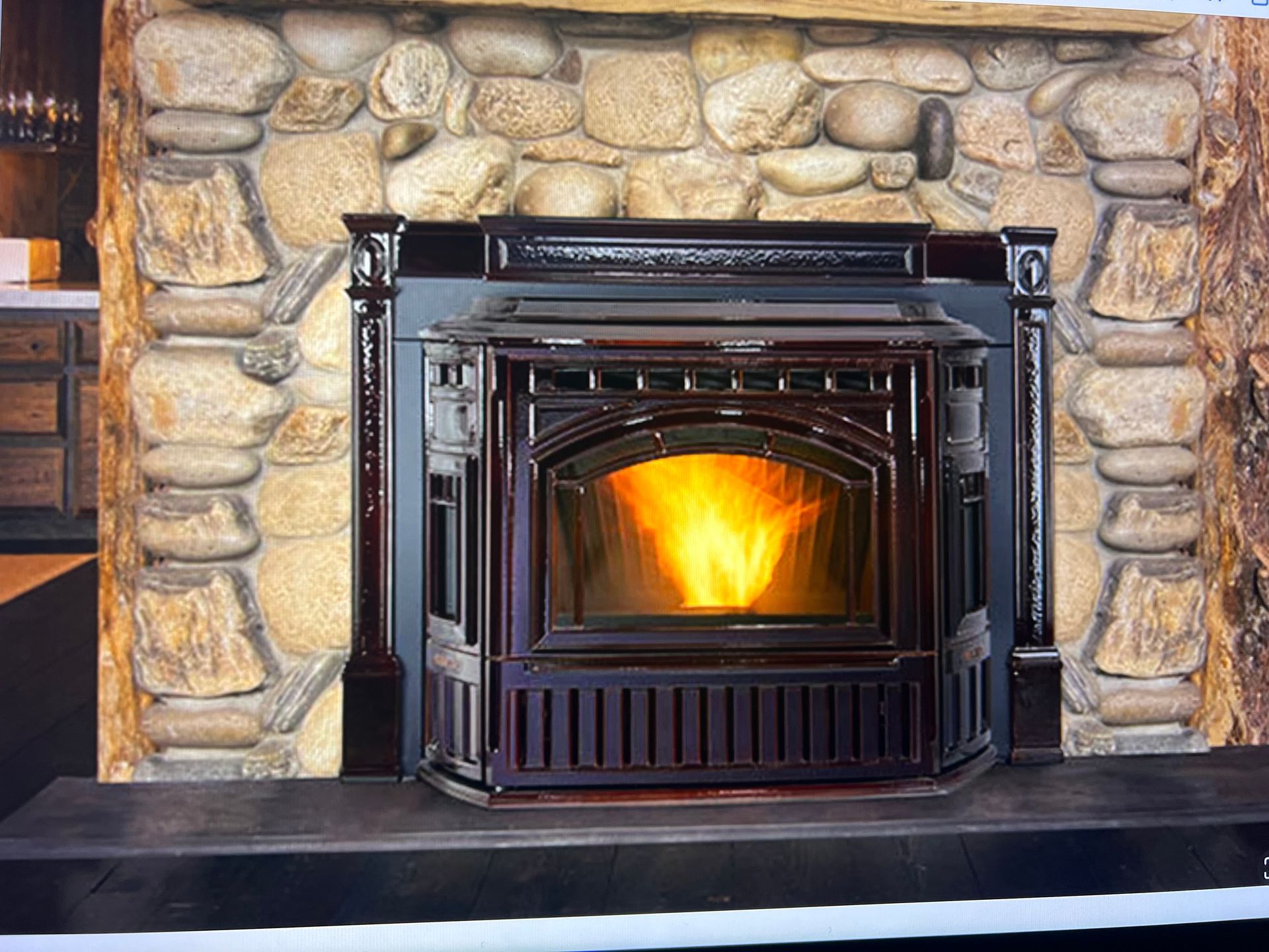 A dark maroon pellet fireplace insert with a glowing orange fire, set into a stone hearth and wall.
