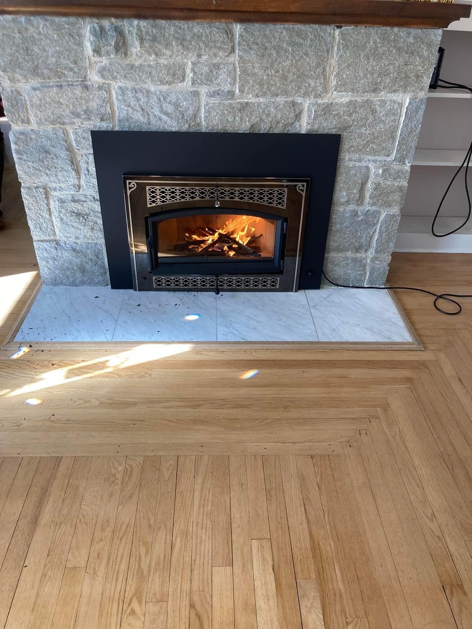 A stone fireplace with a glowing fire insert, set above light-colored wood flooring and a gray hearth.