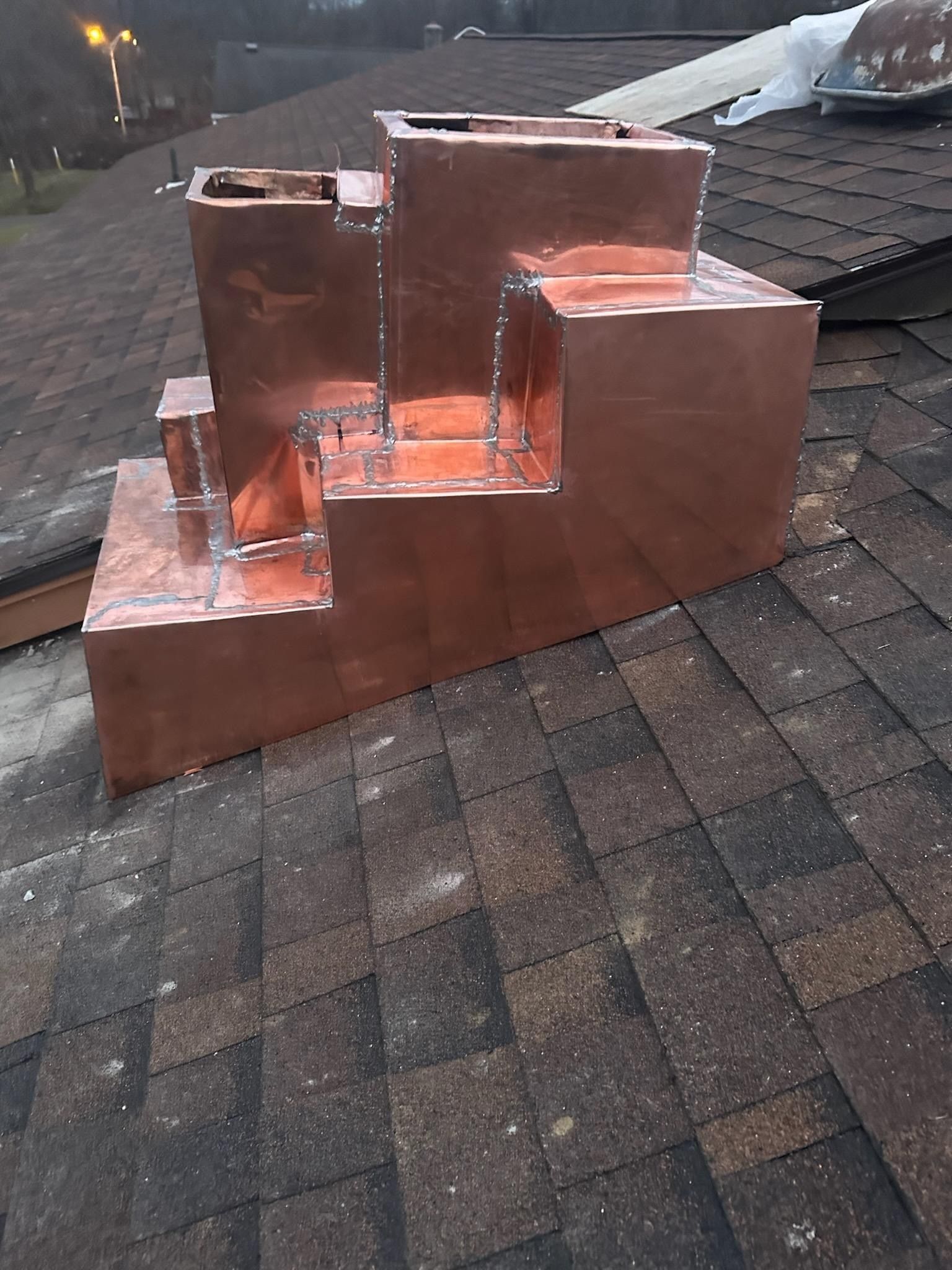 Copper chimney flashing installed on a dark shingled roof with several tiered sections.