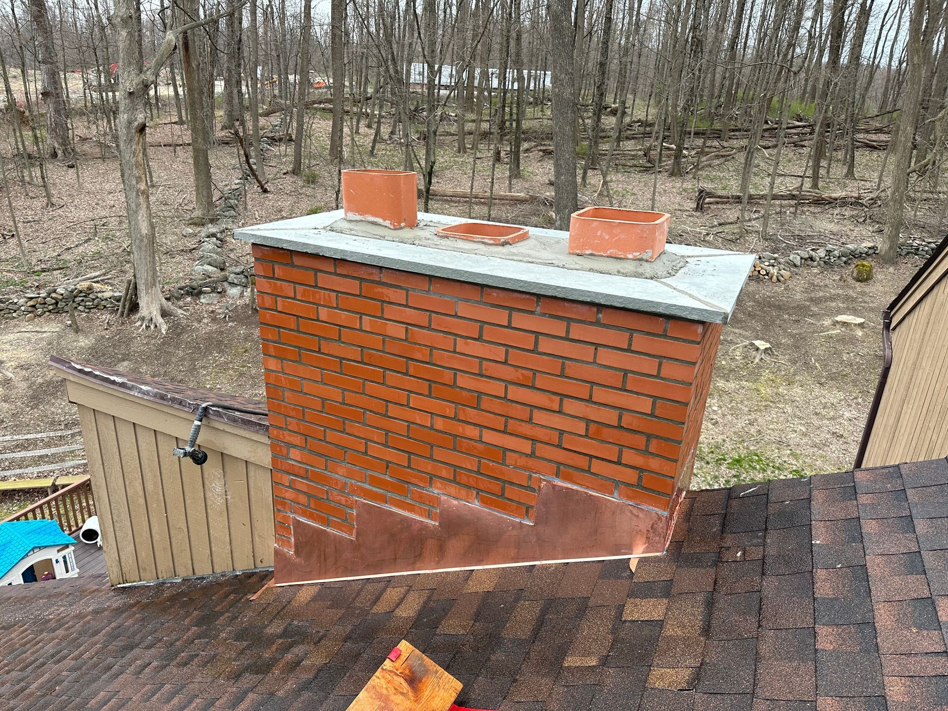 A brick chimney on a shingled roof with copper step flashing installed against the side.