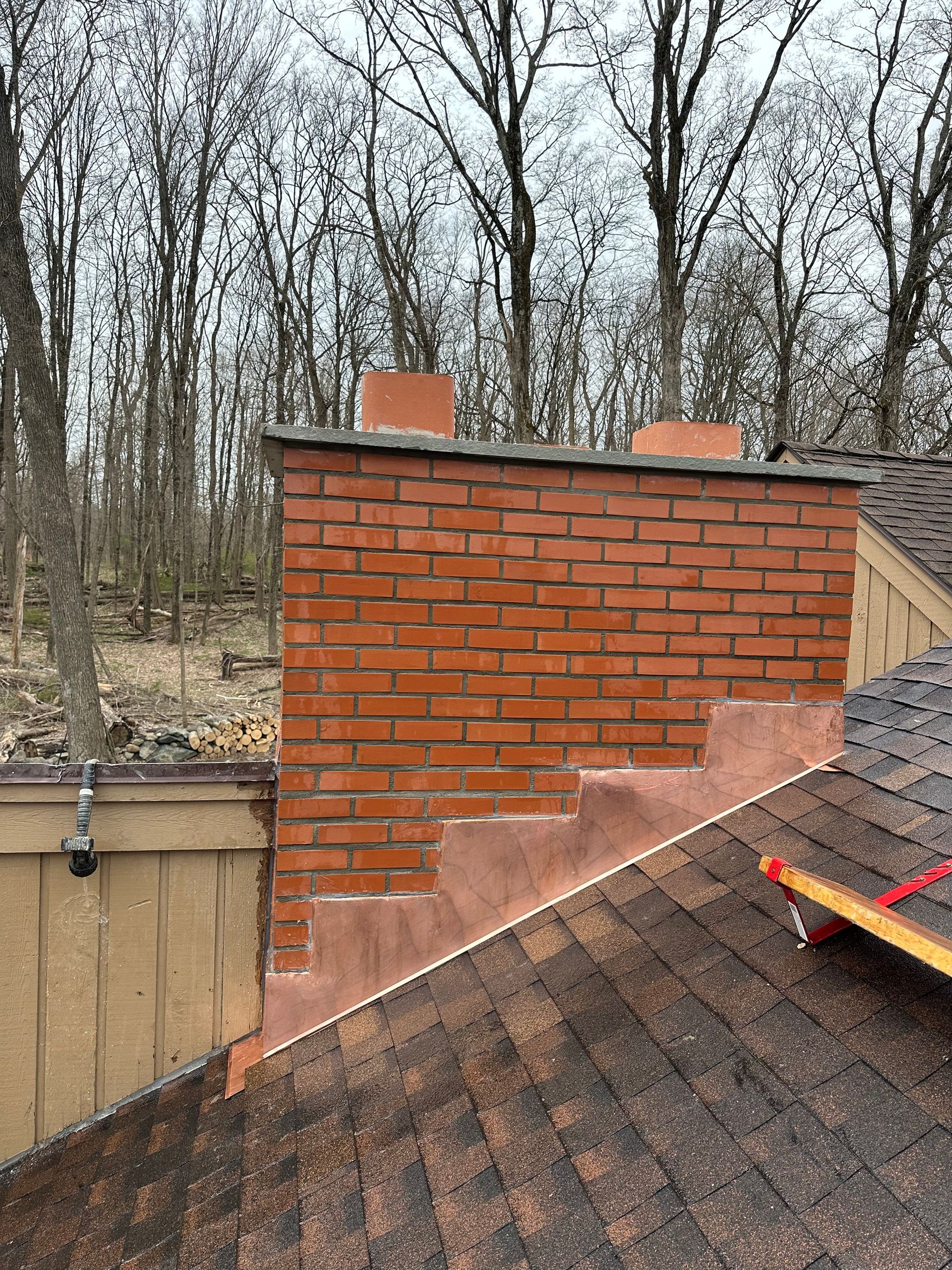 A red brick chimney on a shingled roof with recent mortar repairs along the stepped flashing.