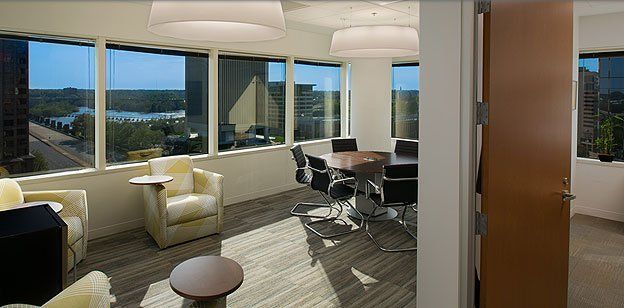 Modern office meeting room with city views. Round table, black chairs, and armchairs by the windows.