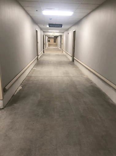 Long, empty hospital hallway with doors on either side and overhead lighting.