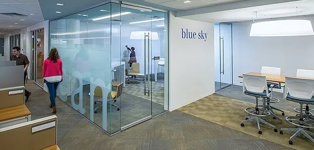 Office interior with glass walls, conference room, and people walking by. 