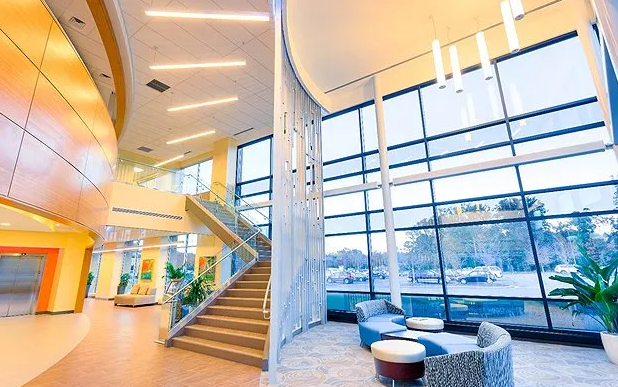 Modern building interior with large windows, curved walls, staircase, and seating area.