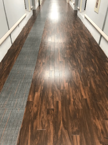 Long hallway with wooden floor, a gray runner, and handrails.