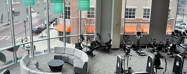 Gym interior with exercise machines, a round sofa, and a city view.