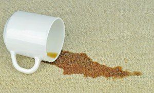 White mug overturned, spilling brown liquid onto a beige carpet.