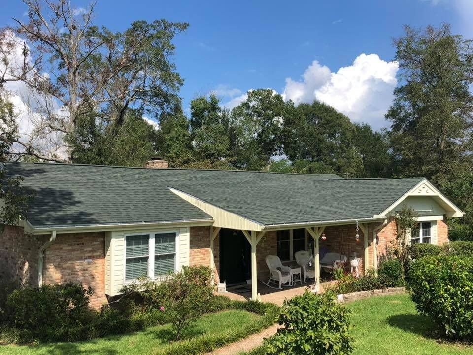 Single-story brick house with green roof, covered porch, and front lawn under a blue sky