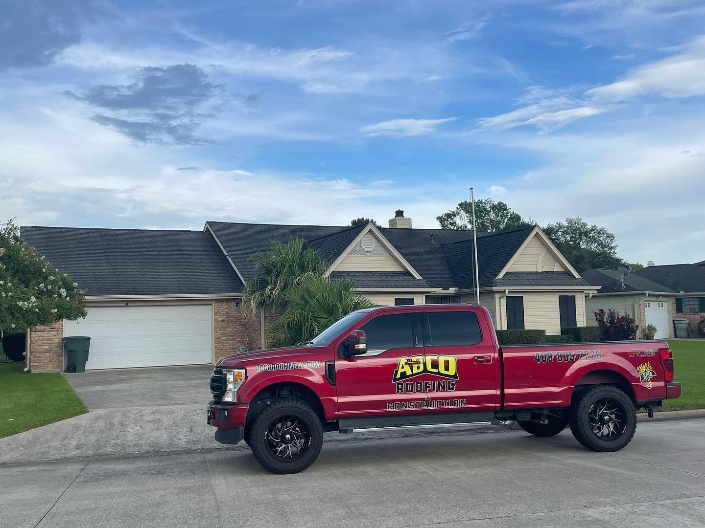 Red utility pickup truck parked in front of a suburban house under a blue sky