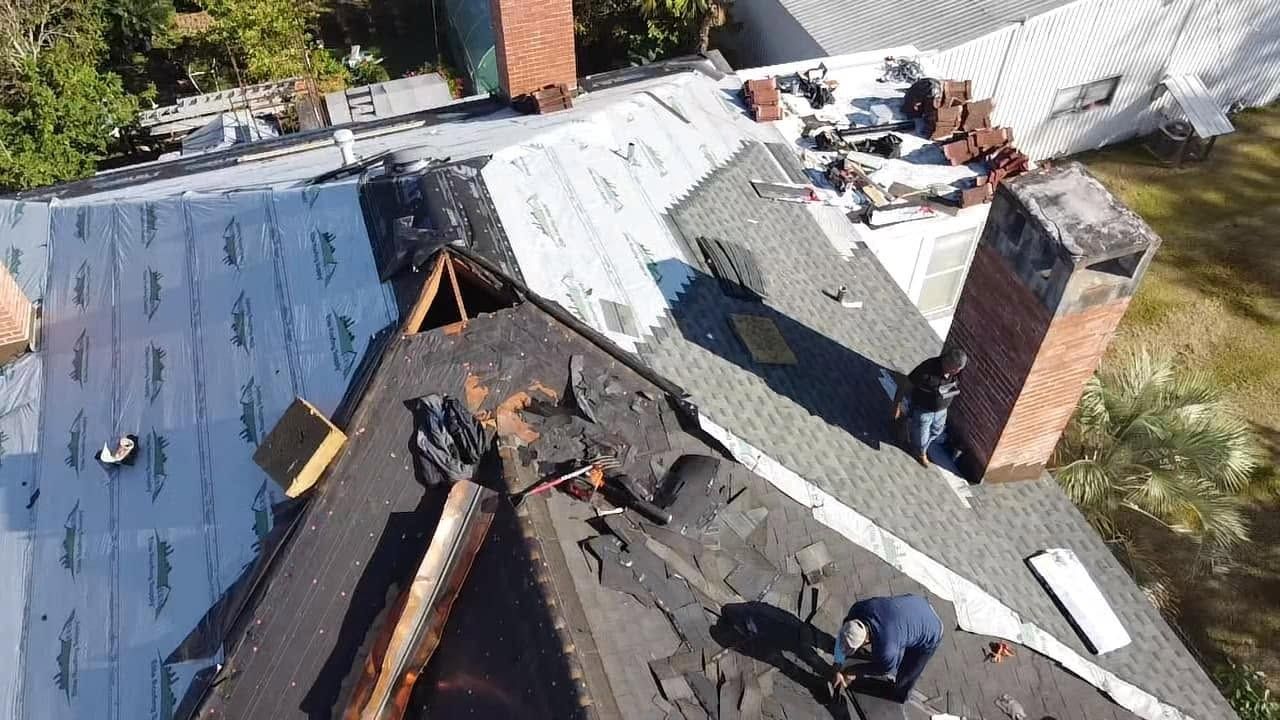 Roofing crew repairing a house roof with new shingles and materials spread across the rooftop.