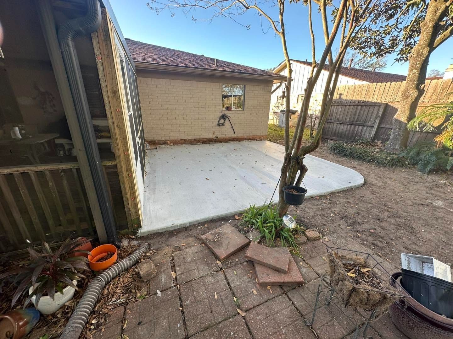 Backyard patio with concrete slab, potted plant, brick walkway, and a beige garage wall