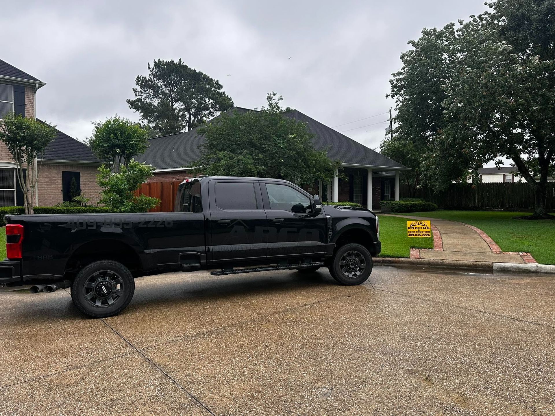 Black pickup truck parked on a gravel driveway in front of a house with a lawn and cloudy sky