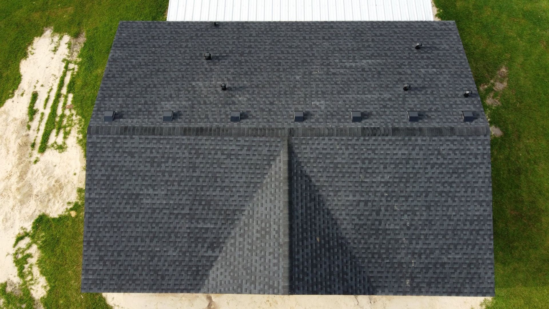 Aerial view of a dark gray shingled house roof with vents and a central front peak.