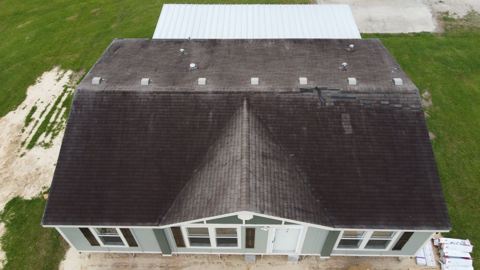 Aerial view of a house with a dark shingle roof and light exterior, surrounded by green grass.