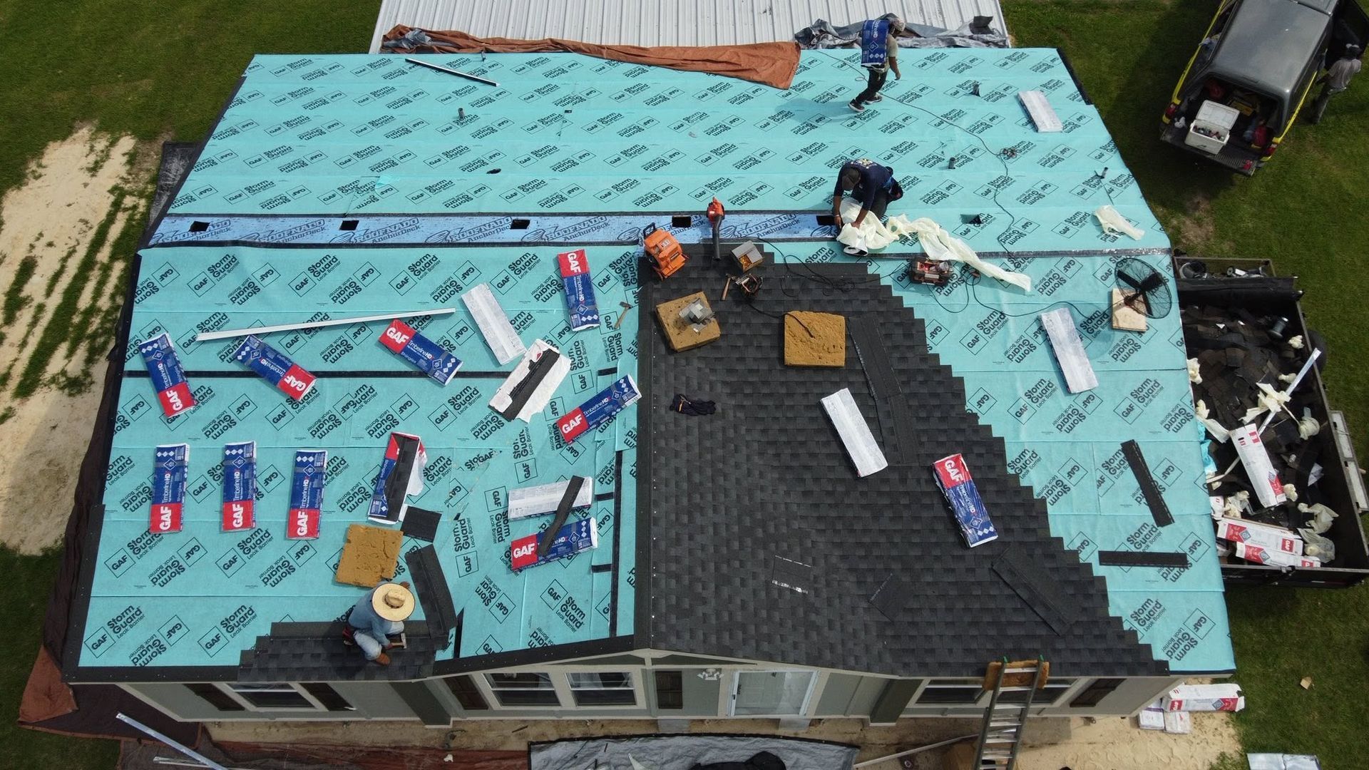 Aerial view of workers repairing a turquoise roof with scattered materials and tools.