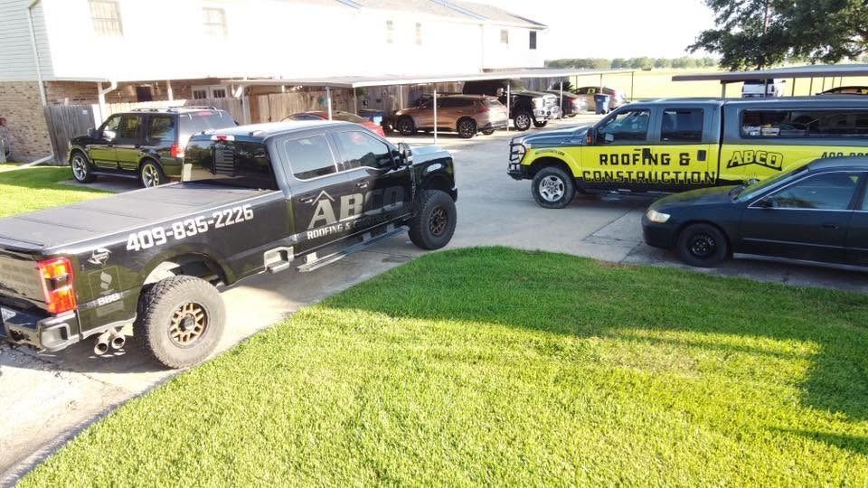 Two race cars parked on grass beside a garage, one black and one yellow with a trailer.