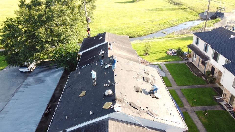 Aerial view of a damaged apartment roof with debris, beside a grassy yard and sidewalk.