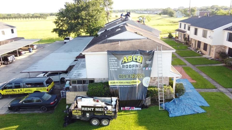 Aerial view of a roof repair crew working on a townhouse with roofing signs and equipment below.