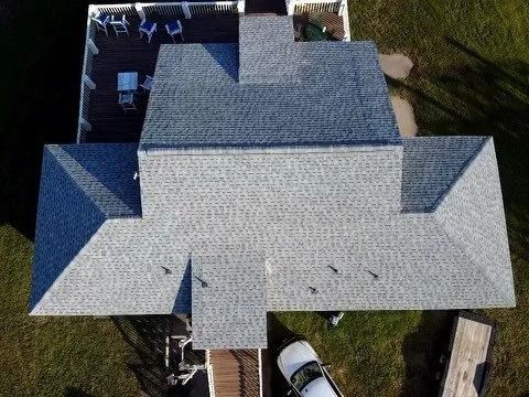 Aerial view of a gray roof on a house with a white car parked below and grassy yard around it