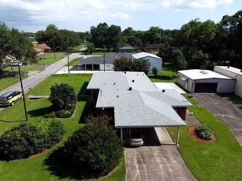 Aerial view of a suburban home with a gray roof, driveway, lawn, and detached garage under a sunny sky