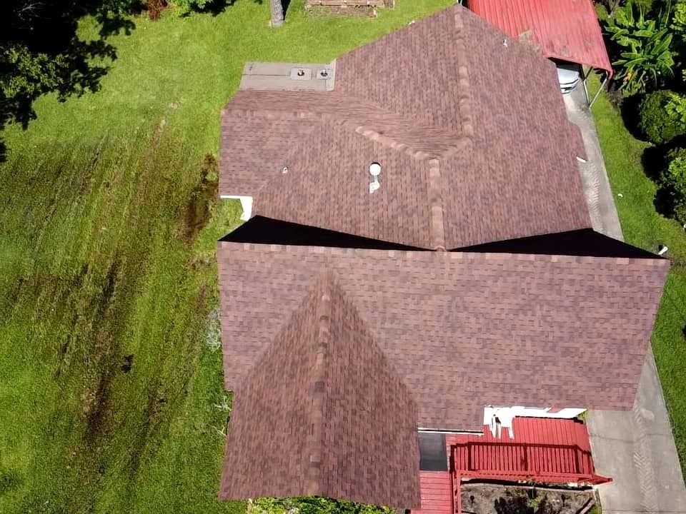 Aerial view of a brown-roofed house with a red porch, surrounded by green lawn.