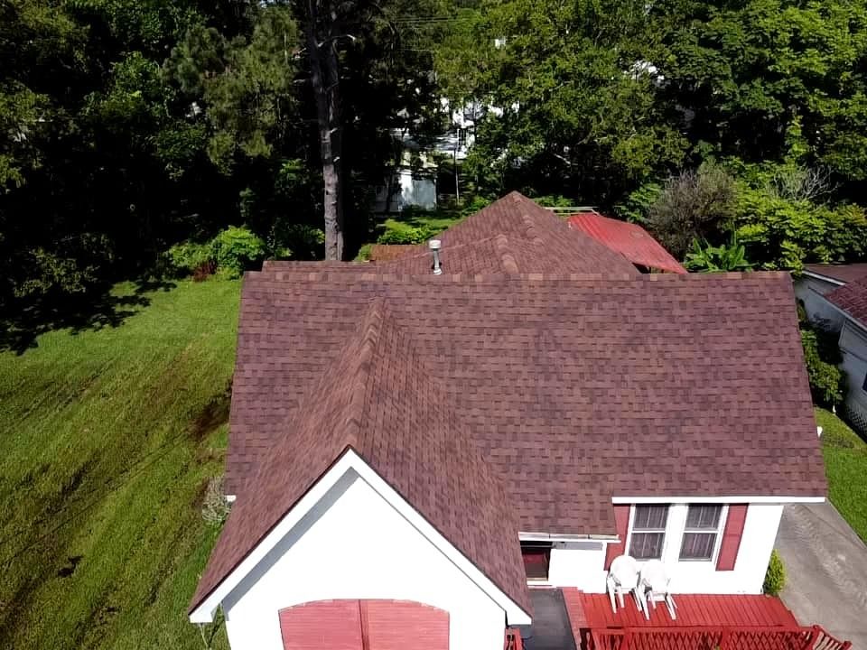Aerial view of a white house with a brown roof beside a steep grassy hillside and trees
