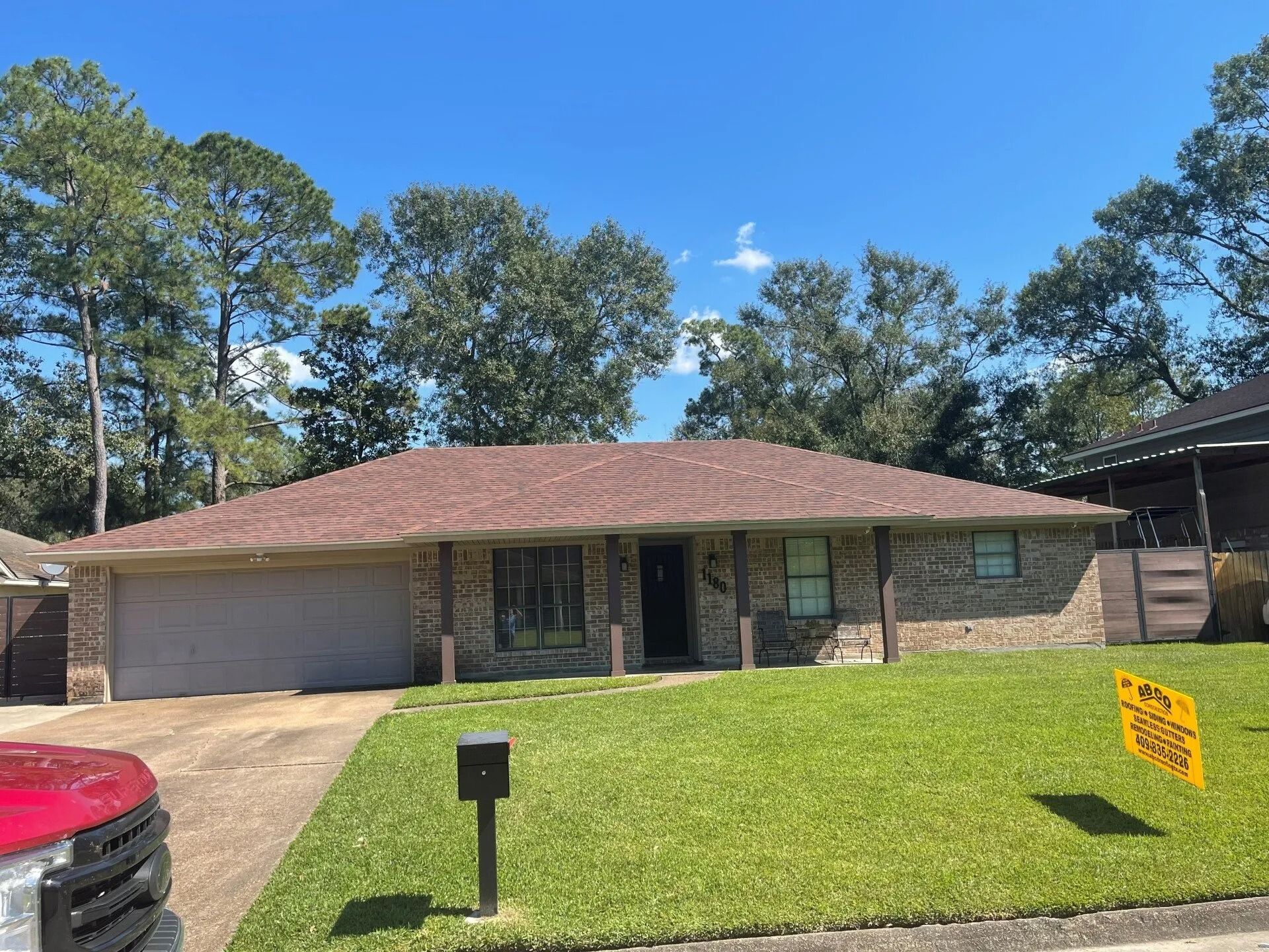 Single-story brick house with a two-car garage, front lawn, and a for-sale sign in the yard