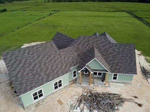 Aerial view of a new green house with a dark roof beside a pile of construction debris.