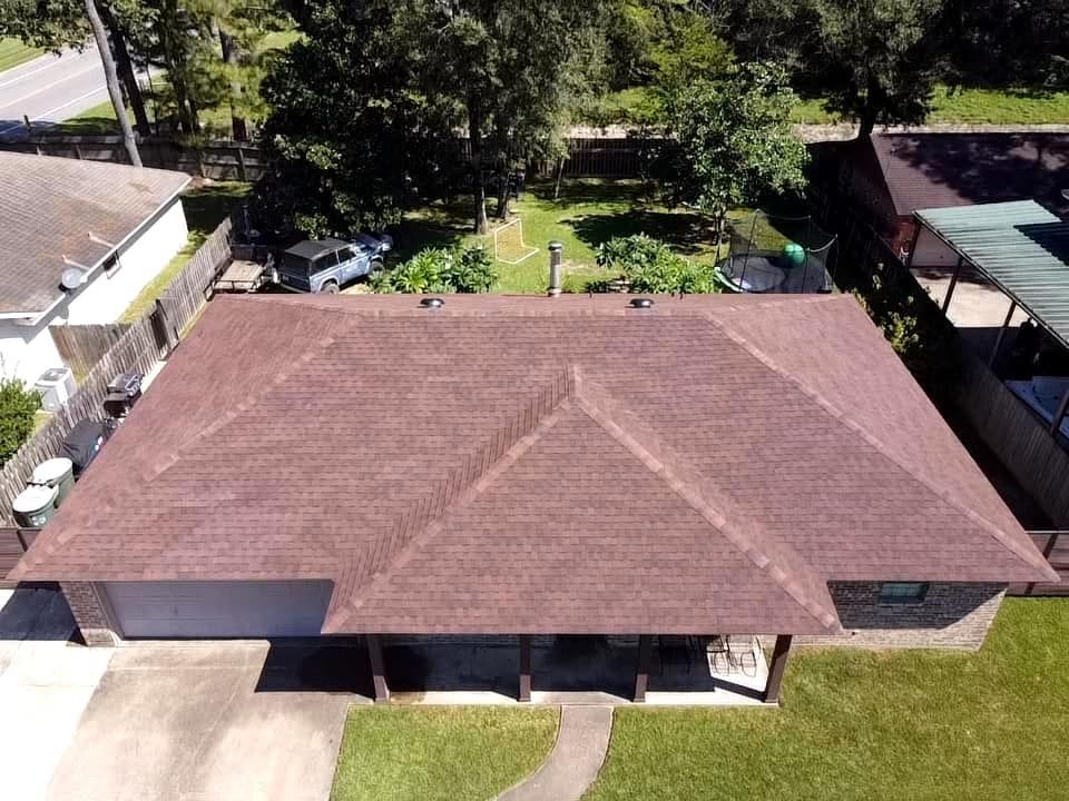 Aerial view of a brown-roofed house with a backyard and trees surrounding it.
