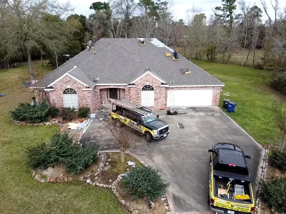 Aerial view of a brick house with driveway, two trucks, and trees in the yard