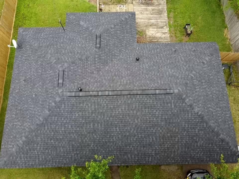 Aerial view of a gray shingled roof with skylights and a vent, bordered by lawns and a driveway.