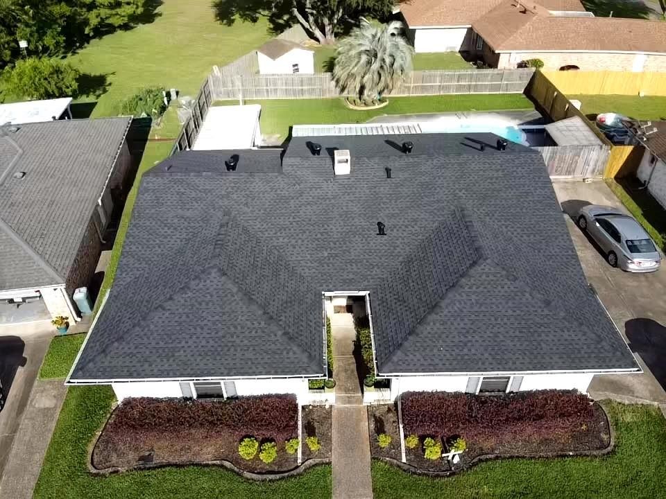 Aerial view of a suburban house with a dark roof, landscaped front yard, and driveway.