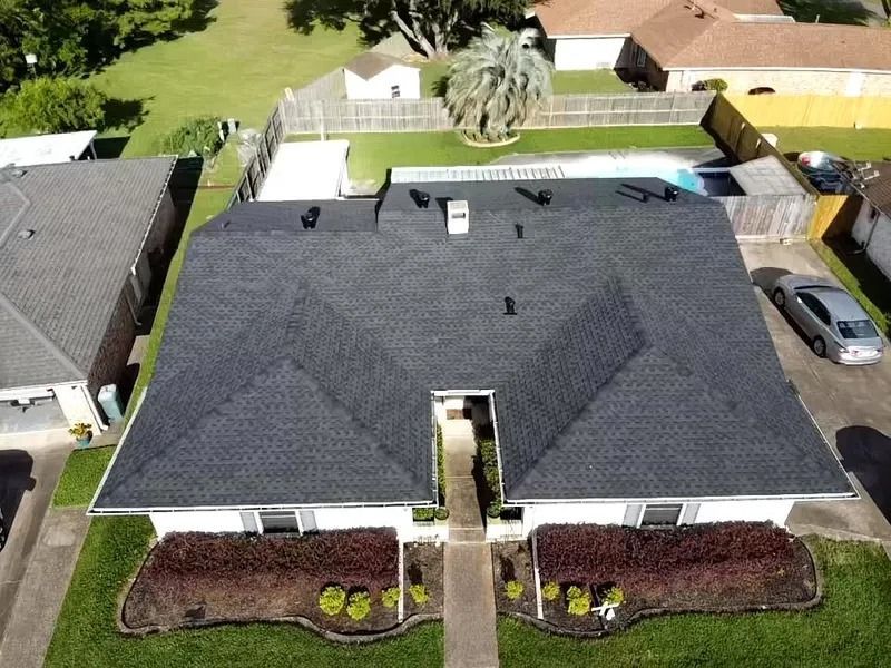 Aerial view of a suburban house with a dark roof, landscaped front yard, and backyard pool.