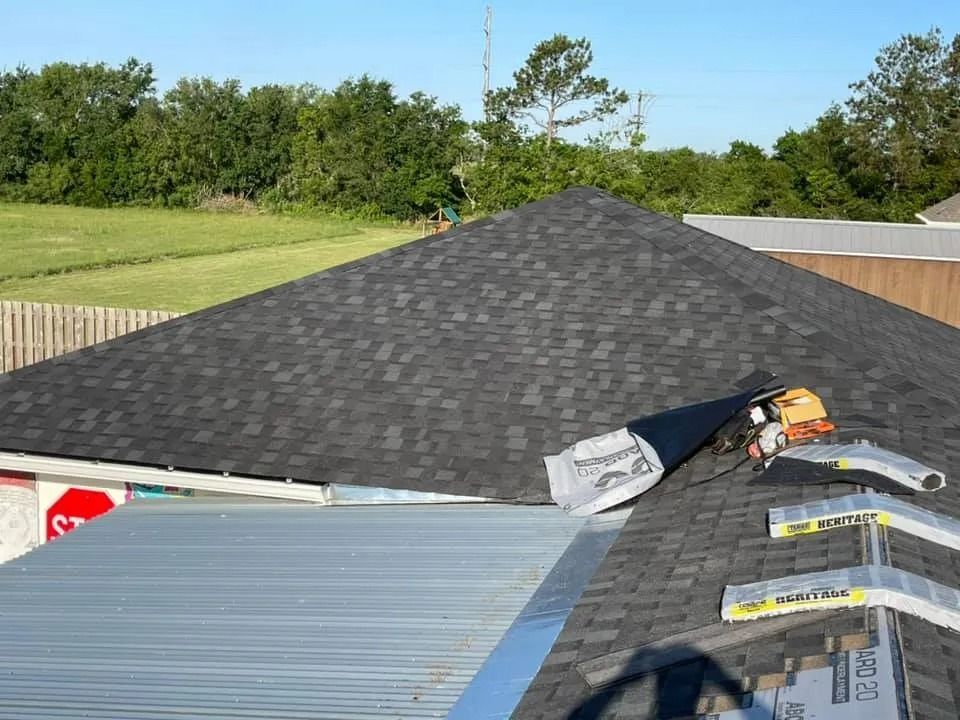 Roof under construction with dark shingles, gray metal roofing, and tools on a sloped house roof.
