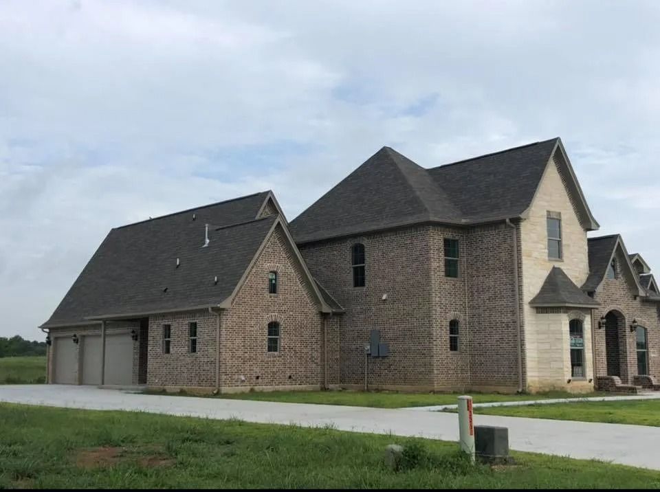 Large brick suburban house with attached garage, dark roof, and arched front entry under cloudy skies