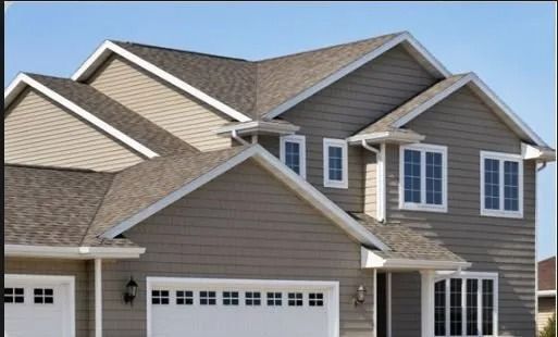 Suburban two-story beige house with white trim, gabled roof, and attached garage under a blue sky