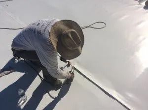 Worker in a hat using a tool to repair a white rooftop seam