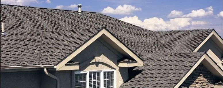 Gray shingled house roof with dormers under a partly cloudy sky