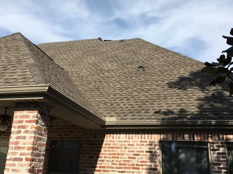 Brick house exterior with shingled roof and windows under a partly cloudy sky