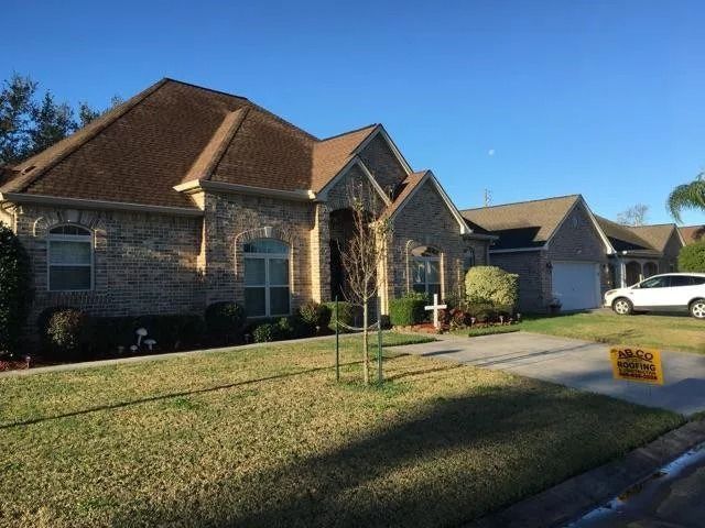 Suburban brick house with a manicured lawn, driveway, and parked car under a clear blue sky